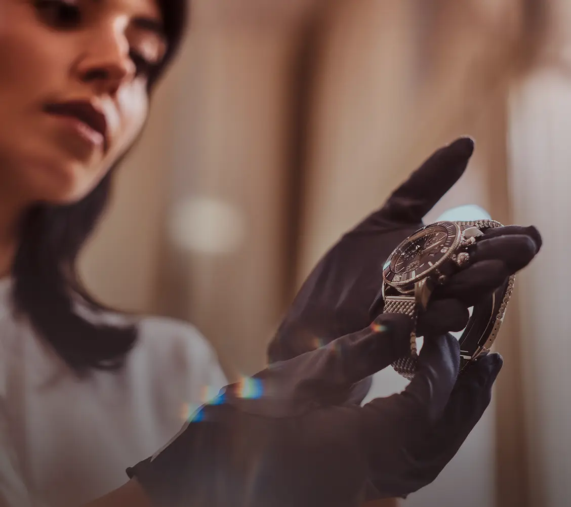 Femme portant des gants noirs examinant une montre-bracelet de luxe en métal avec cadran foncé.